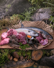 Fish, lamb, organs and mussels arranged on a woven mat