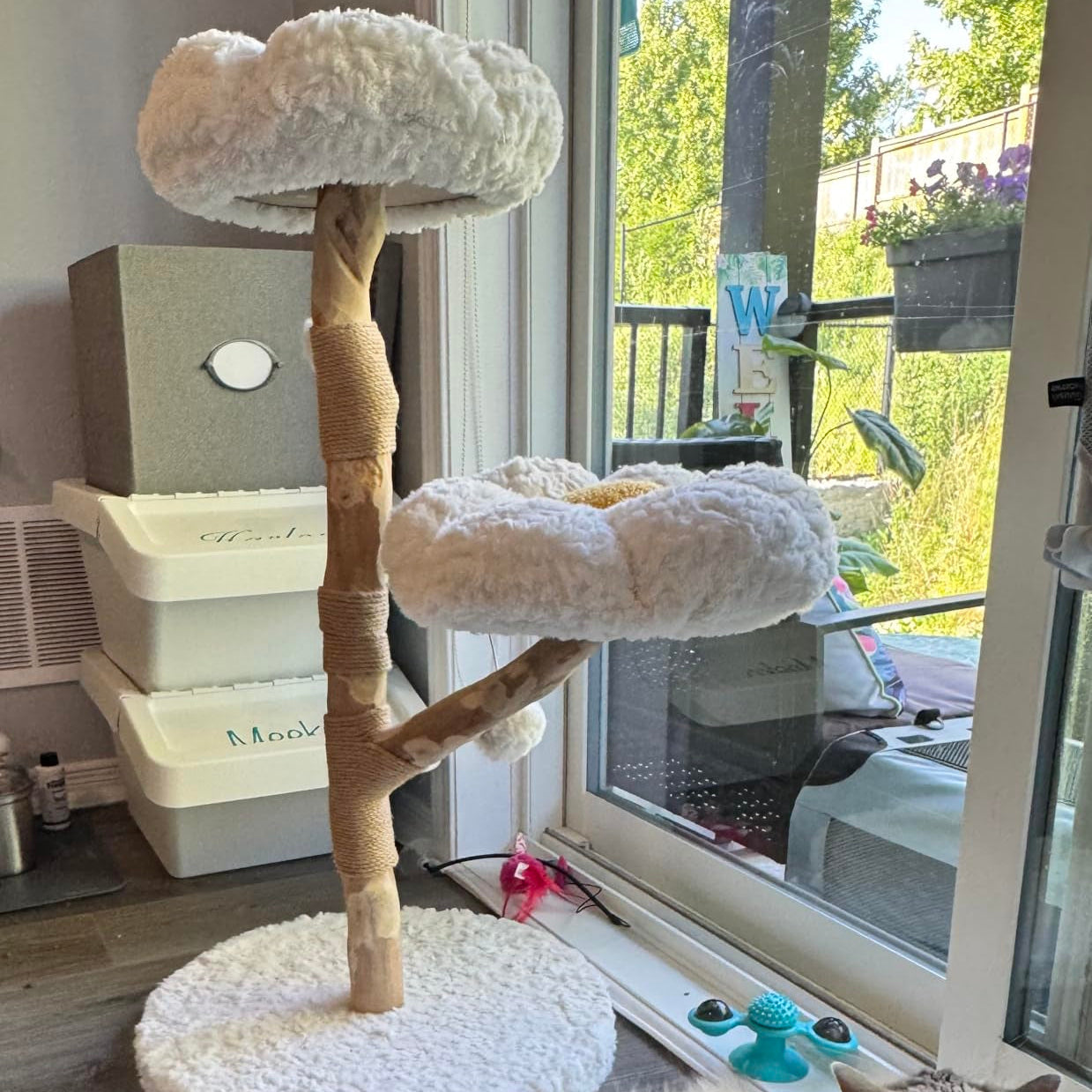 Wooden cat tree with plush flower perches beside a balcony door