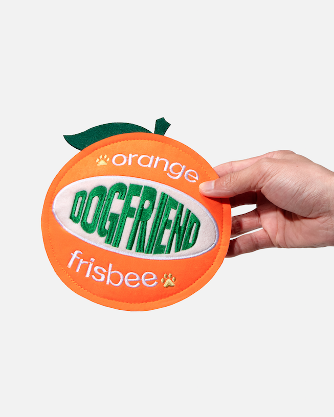 Hand holding an orange-shaped fabric dog flying disc